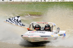 Defending world champion Peter Caughey with the chequered flag at the final round of the jetsprint world champs at Wanganui (photo Ian Thornton)